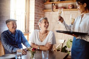 Senior couple, waiter and champagne in restaurant for wedding anniversary, celebration or birthday.